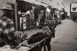 Image du Maroc Professionnelle de  Un chariot tiré par un âne transporte des matériaux de construction dans la rue Sidi El Yamani au quartier Ksour de la Médina de Marrakech. Le commerçant à gauche  expose près du distributeur de carburant mélangeur pour motocyclette des anciennes photos, Dimanche 8 Décembre 2018. (Photo / Abdeljalil Bounhar) 